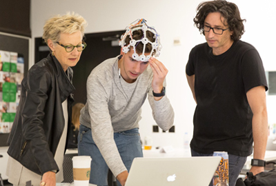 student with instructors, student is wearing sensors on his head and looking at a computer.